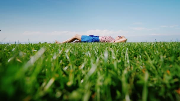 Зеленая лужайка, на которой лежит молодая женщина, смотрит на небо и отдыхает — стоковое видео