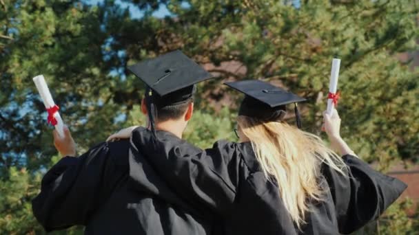 Achteraanzicht van afgestudeerden feliciteren elkaar met het afstuderen aan de universiteit, knuffelen — Stockvideo