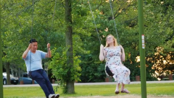 Aktivní mladá rodina odpočívající v parku, jezdit na houpačce. Těhotná žena a asijský muž — Stock video