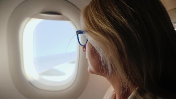 Business woman with glasses flying in an airplane, looking out the window — Stock Video