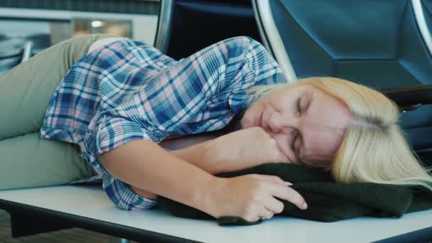 Женщина спит на скамейке в здании терминала аэропорта. Ожидание долгой пересадки на рейс — стоковое видео