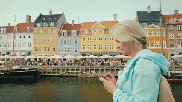 Copenhague, Dinamarca, julho de 2018: Mulher usa smartphone em segundo plano canal Nyhavn, contra o fundo de famosas casas coloridas . — Vídeo de Stock