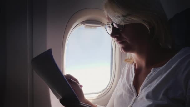 Una joven con gafas lee documentos de negocios en vuelo — Vídeos de Stock