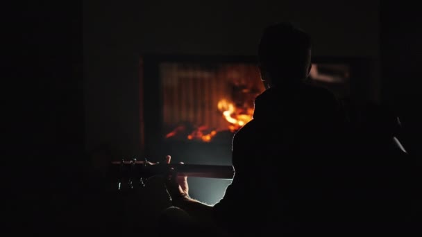 Nastolatek gra na gitarze w ciemności siedząc przy kominku — Wideo stockowe