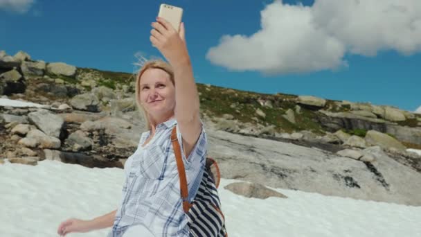Una mujer feliz haciendo selfie en un glaciar en Noruega. Tiempo caluroso, pero la nieve no se ha derretido todavía. La increíble naturaleza de Escandinavia — Vídeo de stock