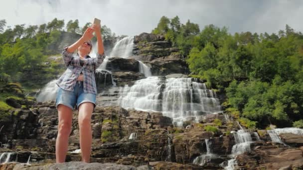 A nő a háttérben fotózza magát Norvégia legmagasabb vízesésénél. Visszanézés — Stock videók