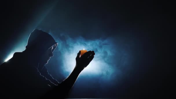 Η σιλουέτα ενός άντρα με κουκούλα, που κρατάει ένα αναμμένο κερί. Μέσα στην ομίχλη που στροβιλίζεται — Αρχείο Βίντεο