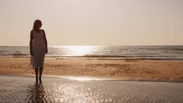 Silueta mladé ženy stojící při západu slunce na pláži — Stock video