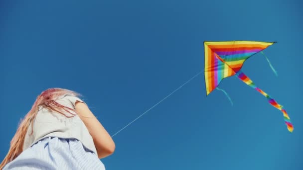 Chica juega con cometa que vuela alto en el cielo azul — Vídeos de Stock