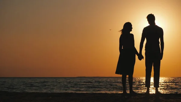 Siluety zamilovaného mladého páru stojícího při západu slunce u moře — Stock fotografie