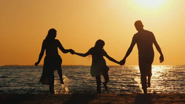 Семья с ребенком развлекается на пляже под лучами заходящего солнца — стоковое фото