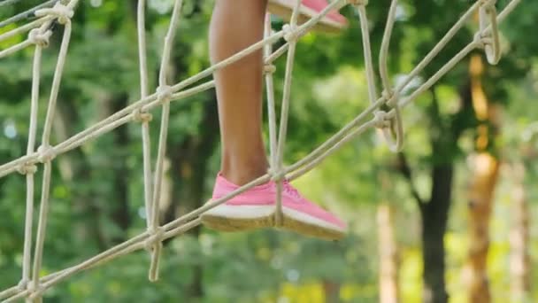 The girl walks on the ropes high in the branches of the tree, in the frame only the legs are visible — 비디오