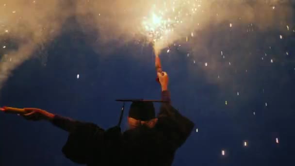 Um graduado universitário emocional em um manto e um boné de graduação com dois fogos de artifício em suas mãos — Vídeo de Stock