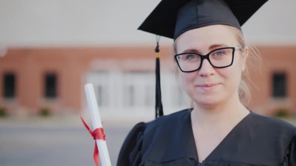 Porträt einer Absolventin mit Mütze und Mantel auf dem Hintergrund eines Hochschulgebäudes — Stockvideo