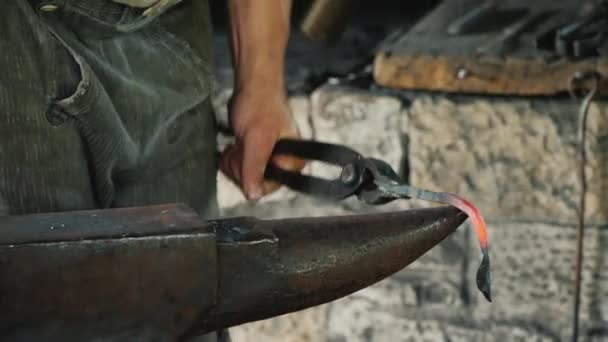 Un herrero hace un producto de hierro, golpea el yunque con un martillo. Artesanía antigua — Vídeo de stock