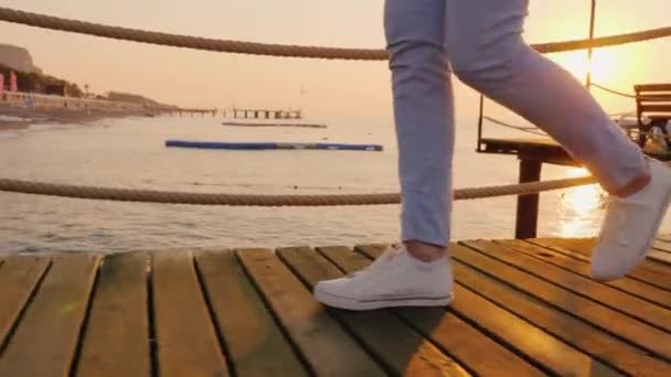 Una mujer camina sobre un muelle de madera sobre el mar, en el marco solo las piernas son visibles — Vídeo de stock