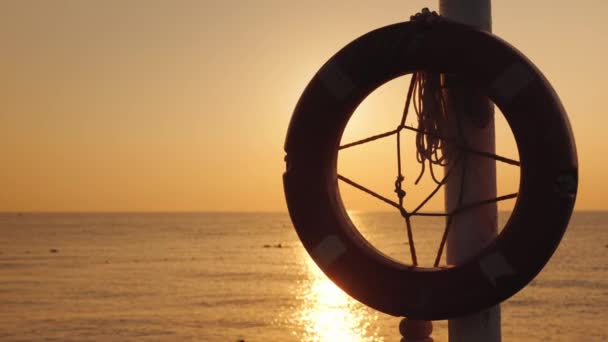 Uma tábua de salvação pendura contra o pano de fundo do mar onde o sol nasce — Vídeo de Stock
