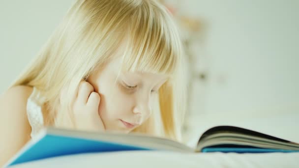 Malá blondýnka čte knihu v posteli. — Stock video