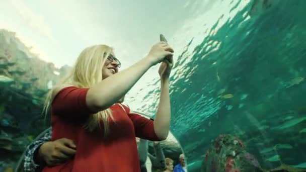 Toronto, Kanada, 2017. október: Egy fiatal, többnemzetiségű pár csodálja a halakat az akvárium üvegalagútjában. Egy nő okostelefonnal fotózza őket. — Stock videók