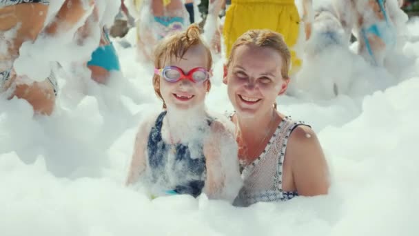 Una joven con un niño completamente envuelto en espuma mira a la cámara y sonríe — Vídeo de stock