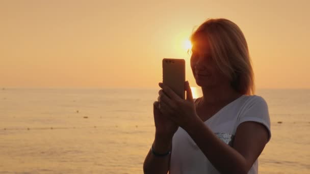 die Silhouette einer Frau, die sich vor dem Hintergrund der über dem Meer aufgehenden Sonne fotografiert