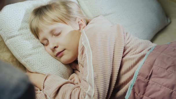 Una mujer pone su mano en la frente de un niño dormido, comprueba la temperatura — Vídeos de Stock