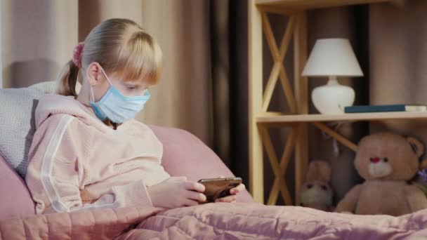 Girl in a gauze bandage plays on a smartphone. Quarantine and root ingesthes at home concept — Stok video