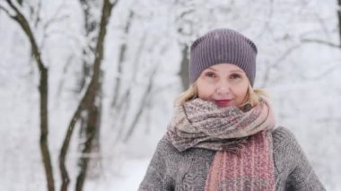 Portrait of a woman in a warm sweater and scarf, stands against the background of a snow-covered winter park