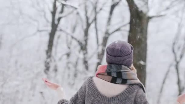 Egy fiatal nő örül a tél érkezésének, forog és hópelyheket fog a téli parkban. — Stock videók