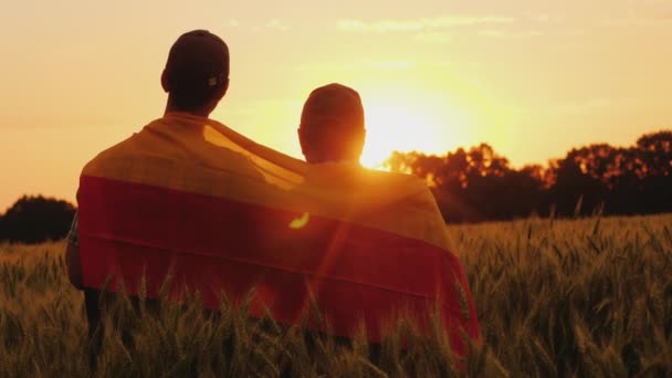 Dois homens com a bandeira da Alemanha atrás dos ombros estão num lugar pitoresco num campo de trigo. — Vídeo de Stock