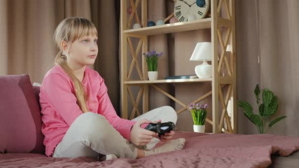 El niño juega un videojuego, se sienta en su cama con un joystick — Vídeos de Stock