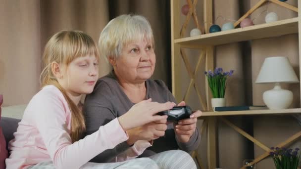 Ребенок учит свою бабушку играть в видеоигры на игровой консоли — стоковое видео
