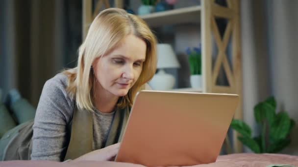 Portret kobiety w średnim wieku leżącej na łóżku w sypialni korzysta z laptopa — Wideo stockowe