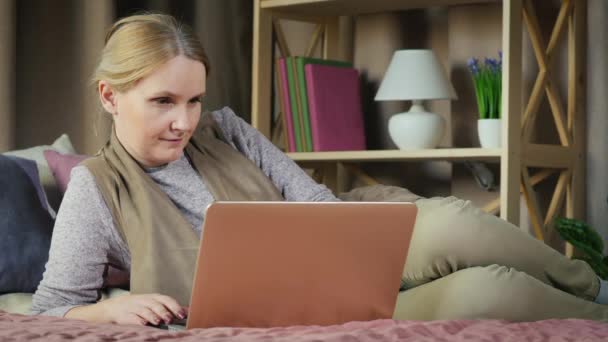 Una mujer de mediana edad usa un portátil en su cama — Vídeos de Stock