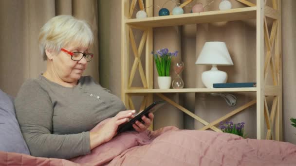 Mujer mayor se relaja en su habitación, utiliza tableta — Vídeo de stock