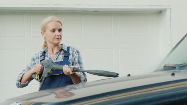 Портрет активной женщины, моющей машину возле гаража — стоковое видео