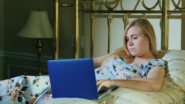 Молодая женщина с ноутбуком отдыхает в постели в своей спальне — стоковое видео