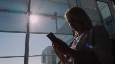 Bir kadın havaalanı terminalinde akıllı telefon kullanarak uçağını bekliyor.