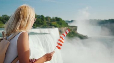 Amerika 'da seyahat eden, elinde Amerika bayrağı olan bir kadın Niagara Şelalesi' ne hayran, Amerika 'nın en ünlü eğlencelerinden biri.