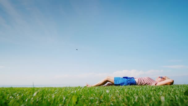 Heureuse femme pieds nus se trouve au milieu d'une prairie verte, rêve et regarde vers le ciel — Video