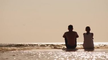 Bir adam ve bir kadın sahilde yan yana otururlar.