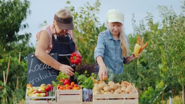 子供を持つシニア大人の女性は、農産物市場のカウンターに野菜を置きます. — ストック動画