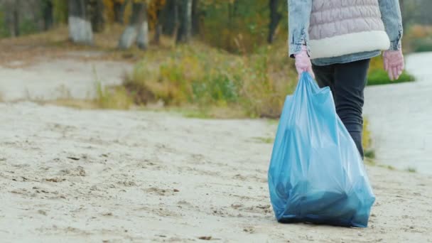 La chica lleva una bolsa pesada con basura. Limpieza de parques y cuidado ambiental — Vídeos de Stock