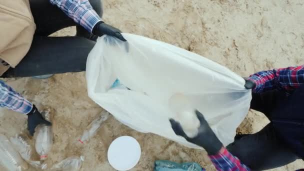 Ovanifrån av Volontärer sätta plast skräp i en påse. Städning av stranden, miljövård. — Stockvideo