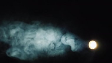 Dar bir ışınla stüdyonun ışıklandırma cihazı karanlıkta dumanı aydınlatıyor.