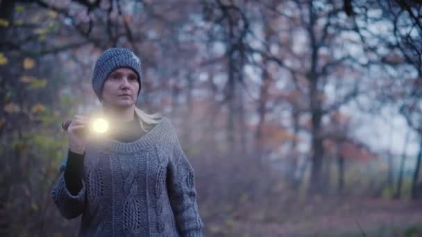 Buscar en el bosque - Una mujer con una linterna camina al atardecer a lo largo de un camino en un bosque denso — Vídeo de stock