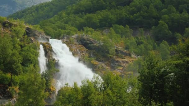 Águas da cachoeira, no fundo da ponte à distância. Água de fusão das geleiras nas montanhas, o derretimento do gelo da geleira Briksdal — Vídeo de Stock