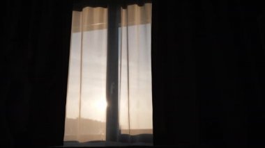 Bir kadının silueti, pencerenin perdesini kapatır.