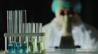 Laboratuvardaki reaktif test tüpleri, arka planda bir adam mikroskop ile çalışır.