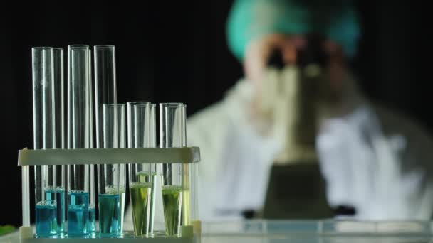 Provette di reagente in laboratorio, sullo sfondo un uomo lavora con un microscopio — Video Stock